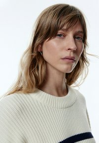 Gebreide trui in off-white, met een gestructureerd patroon. Ribbelboord bij de ronde hals en een marineblauwe horizontale streep over de borst.