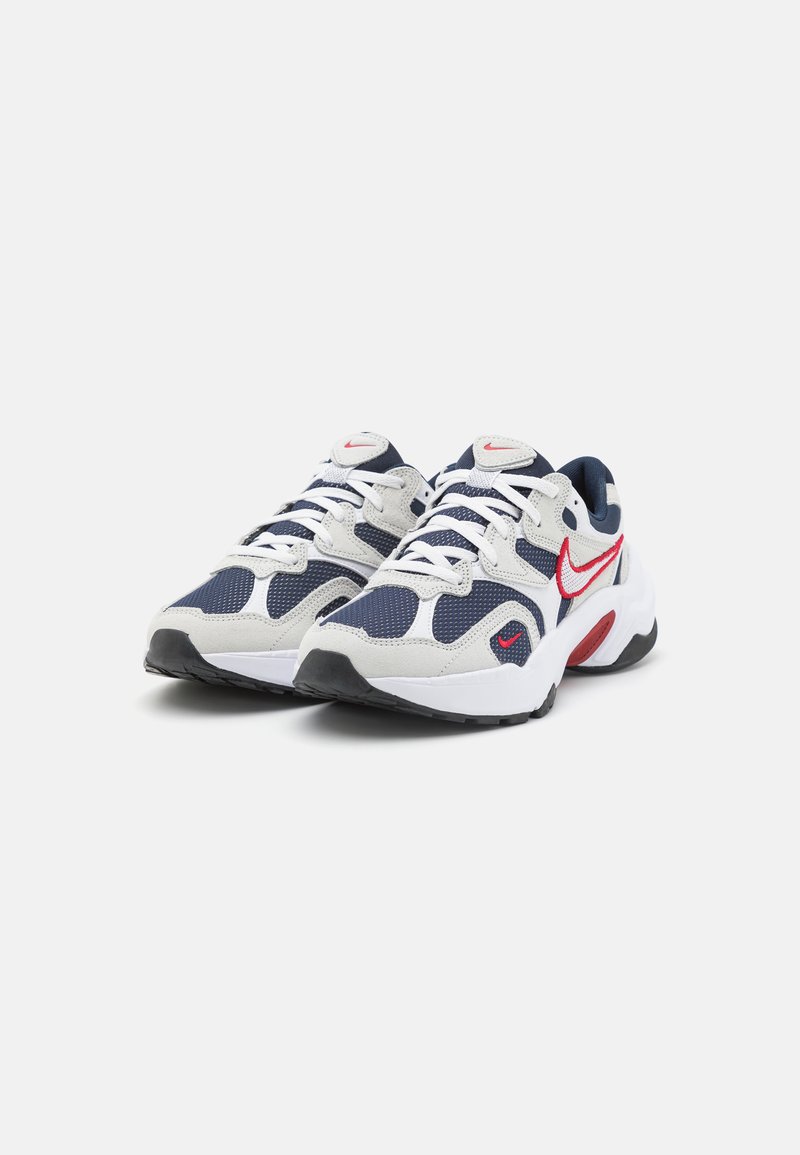 Zapatillas para hombre con parte superior de malla y gamuza en blanco, azul marino y rojo. Presentan cordones blancos, cuello acolchado y suela de goma negra texturizada.