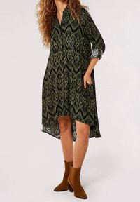 Grünes gemustertes Kleid mit Kragen, langen Ärmeln, die an den Manschetten gerollt sind, und seitlichen Taschen. Es hat einen asymmetrischen Saum und geometrische Designdetails.