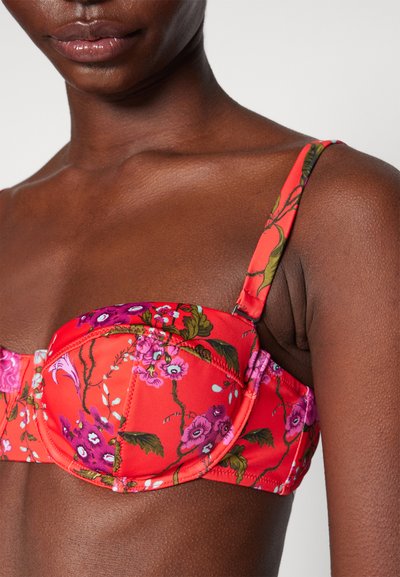 Red floral print bra with adjustable straps, featuring padded cups and textured fabric. Floral patterns include pink and green accents.