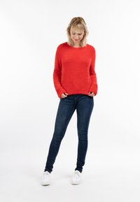 Rode fluffy trui met lange mouwen, ronde hals en een gestructureerde afwerking, gecombineerd met donkerblauwe skinny jeans en witte sneakers.