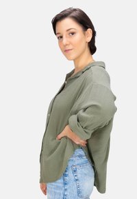 Olive green textured button-up shirt with a loose fit and long sleeves, paired with light blue high-waisted denim jeans.