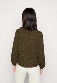 Blusa verde-oliva escuro com padrão preto manchado, mangas longas e decote redondo. Tecido leve, ajuste semi-solto e punhos franzidos.