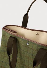 Πράσινη τσάντ�α ώμου από μάλλινη ύλη με καφέ πλεκτές λαβές, μπεζ επένδυση εσωτερικά και άκρη με δέρμα, κλεισμένη με μεταλλικό κουμπί ασφαλείας.