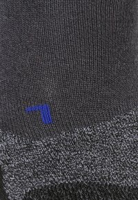 Schwarze Stricksocke mit einem strukturierten Muster. Verfügt über ein kleines blaues Logo-Detail. Das Material wirkt weich und dehnbar.