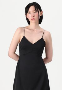 Vestido preto com alças finas e decote em V, apresentando um corpete justo, textura suave e silhueta fluida.