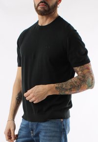 Maglione nero a maniche corte realizzato in tessuto a maglia, con scollatura a girocollo e una finitura testurizzata sottile. Presenta un piccolo logo sul petto.
