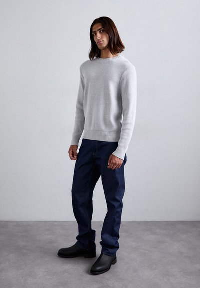 Lichtgrijze gebreide trui met ribbelzoom, gecombineerd met donkerblauwe rechtgesneden jeans en zwarte leren enkellaarzen. Eenvoudig, modern ontwerp.