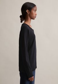 Czarna koszula z długim rękawem i zaokrąglonym dekoltem, z subtelną fakturą i luźnym krojem. W połączeniu z ciemnymi jeansami.