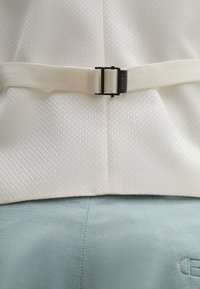 Weißer, strukturierten Stoff mit geometrischem Muster, versehen mit einer hellgrauen Gürtelschnalle mit "JOOP!"-Markierung. Darunter glatter blauer Stoff.