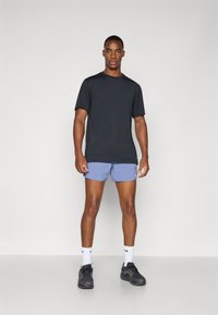 Musta lyhythihainen t-paita, vaaleansiniset shortsit, harmaat lenkkarit, valkoiset sukat mustilla yksityiskohdilla. Yksinkertainen, urheilullinen muotoilu, ei kuvioita.