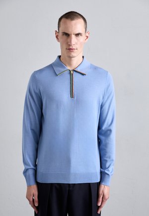 Ljusblå långärmad polo med dragkedja som har en flerfärgad randig accent på kragen. Mjuk, stickad textur.