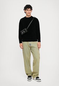 Black knit sweater, loose light green striped pants, black crossbody bag with silver accents, and black sneakers with white stripes.