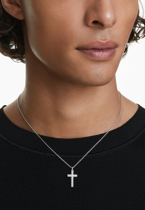 Collana d'argento con pendente a croce, caratterizzata da piccole decorazioni. Il modello indossa un maglione nero, che mette in evidenza il colletto e il dettaglio della catena.