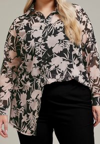 Genomskinlig skjorta med knappar och blommönster i svart och rosa, med krage, långa ärmar och rundad nederkant. Svarta byxor synliga.