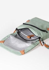 Borsa verde, con texture morbida e dettagli in pelle marrone chiaro, chiusura con zip e interno foderato grigio; presenta una tasca esterna con zip e una tracolla regolabile.