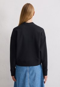 Sweatshirt noir court avec un col rond, texture douce et poignets côtelés. Assorti à une jupe en denim, montrant un design simple et décontracté.