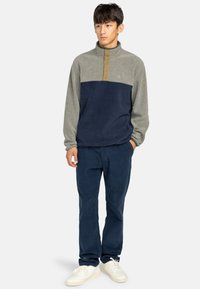 Fleece pulovr s čtvrtinovým zipem v šedé a námořnické barvě, s knoflíkovým výstřihem a měkkou texturou. V kombinaci s tmavě námořnickými kalhotami a bílými teniskami.