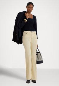 Jasnożółte dzwony z widocznymi przeszyciami i metalowymi guzikami. W zestawie z granatową bluzką z długim rękawem oraz teksturowaną czarno-szarą torebką.