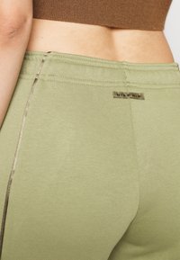 Gröna bomullleggings med en slät textur, prydda med en sidoflik av guldton och en märkesetikett med texten "NIKE AIR" på baksidan.