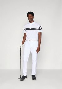 Vit golfpolo med svarta horisontella ränder, kombinerad med vita byxor och svarta golfskor. Handskar och golfklubba ingår.