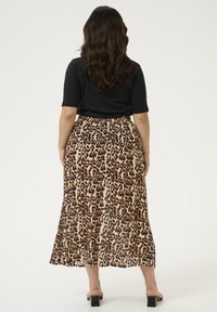 Jupe maxi en imprimé léopard avec un design fluide, arborant un fond beige et des taches marron foncé. Associée à un haut ajusté noir.