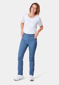 Hellblaue, figurbetonte Hose mit einem Knopf und einem Reißverschluss vorne, kombiniert mit einem kurzärmligen weißen Oberteil und weißen Sneakers.