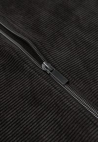 Schwarzer, gerippter Stoff mit einer Nahaufnahme eines glänzenden schwarzen Metallreißverschlusses, der teilweise geöffnet ist.