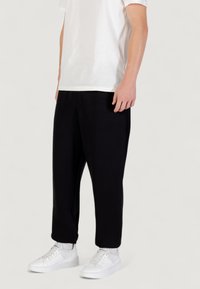 Zwarte joggingbroek gemaakt van zachte stof, met een relaxte pasvorm, zijzakken en elastische boorden, gecombineerd met witte platte sneakers.