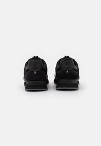 Schwarze Sport Schuhe mit einem strukturierten Mesh-Obermaterial, gepolstertem Schaft und Gummisohle. Sie verfügen über ein elegantes Design und eine Markenlogo an der Ferse.