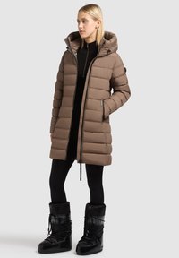 Brown, puffy parka with a hood, zippered front, and side pockets. Paired with black, rugged snow boots. Solid color, sleek design.