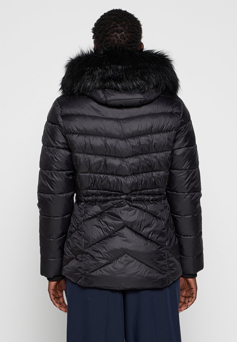 Schwarze Daunenjacke mit Kapuze aus Kunstfell, elastischem Bund und einem Chevron-Steppmuster auf dem Rücken. Glatte Textur und leichtes Design.