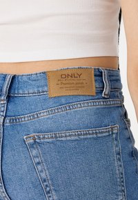 Blauwe denim jeans met een gestructureerde stof, met eenbruin leren label op de tailleband en klassieke stiksels op de achterzak.