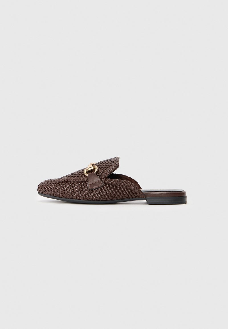 Chaussure slip-on tissée marron avec une semelle plate, présentant un accent en cuir et un détail en métal doré à l'avant. Surface texturée sur l'ensemble.