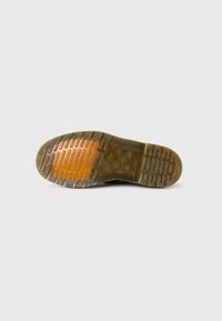 Suela de zapatilla de goma negra con patrón de agarre texturizado; presenta una entresuela transparente con un acento naranja y detalles acanalados.