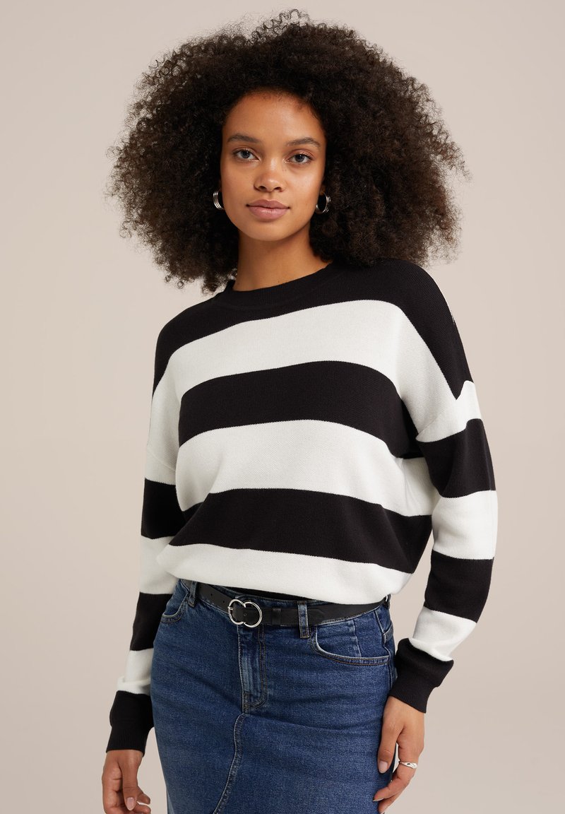 Maglione a righe bianche e nere con colletto a girocollo, spalle cadenti e polsini a costina. Abbinato a una gonna in denim blu e una cintura nera.