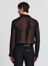 Schwarzes, transparentes Langarmshirt mit spitzem Kragen, kombiniert mit schwarzen, maßgeschneiderten Hosen mit Lederdetails und Seitentaschen.