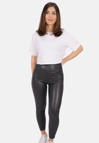 Schwarze, hoch taillierte Leggings aus glänzendem, Kunstleder-Material, kombiniert mit einem weißen, cropped Baumwoll-T-Shirt und weißen Sneakers.