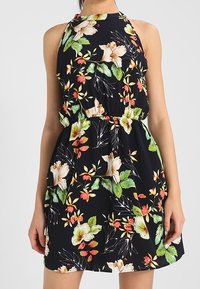 Blommig klänning med halterneck-design, svart bakgrund och färgglada blommönster i grönt, gult, rött och vitt. Lättviktsmaterial.