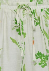 Biely textil s botanickým vzorom v zelenej a oranžovej farbe, s nastaviteľným pásom a mäkkým, textúrovaným povrchom.