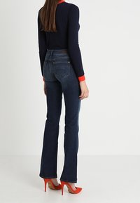 Ciemnoniebieskie dżinsy z szerokimi nogawkami i wysokim stanem, zestawione z dopasowanym granatowym swetrem z czerwonymi akcentami oraz pomarańczowymi szpilkami.