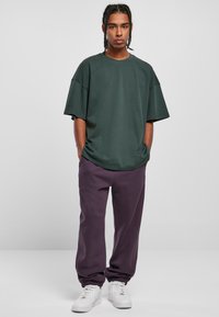 Tricou oversized de culoare verde închis, cu mâneci scurte, asortat cu pantaloni jogger lila, lejeri, cu manșete elastice și adidași albi. Design simplu și casual.