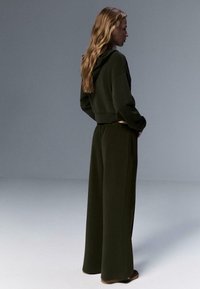 Gekürzter dunkelgrüner Hoodie mit Kapuze, kombiniert mit weitem, passenden Hosen. Weiches Material, lockere Passform und sichtbare Seitentaschen.