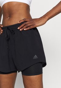 Zwarte sportshorts van een textuurstof met een elastische tailleband, voorzien van zijslitsen en een geborduurd Adidas-logo in het grijs.