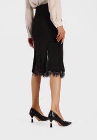 Gonna nera a matita con bordo in pizzo all'orlo, dotata di spacco laterale. Abbinata a tacchi a punta neri, che enfatizzano una silhouette elegante.