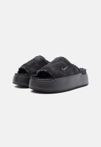 Sandalias de ante negras con la puntera abierta, forro interior acolchado, suela de goma gruesa y un logo metálico de Nike en la parte superior.