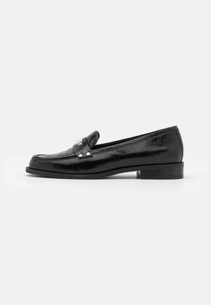 Mocassin en cuir noir avec petit talon et détail métallique doré sur le dessus, présenté en profil latéral sur fond blanc.