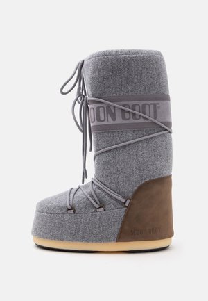 Botte d'hiver haute grise et marron avec une semelle épaisse et des lacets enveloppants, portant le nom de marque Moon Boot sur le côté.