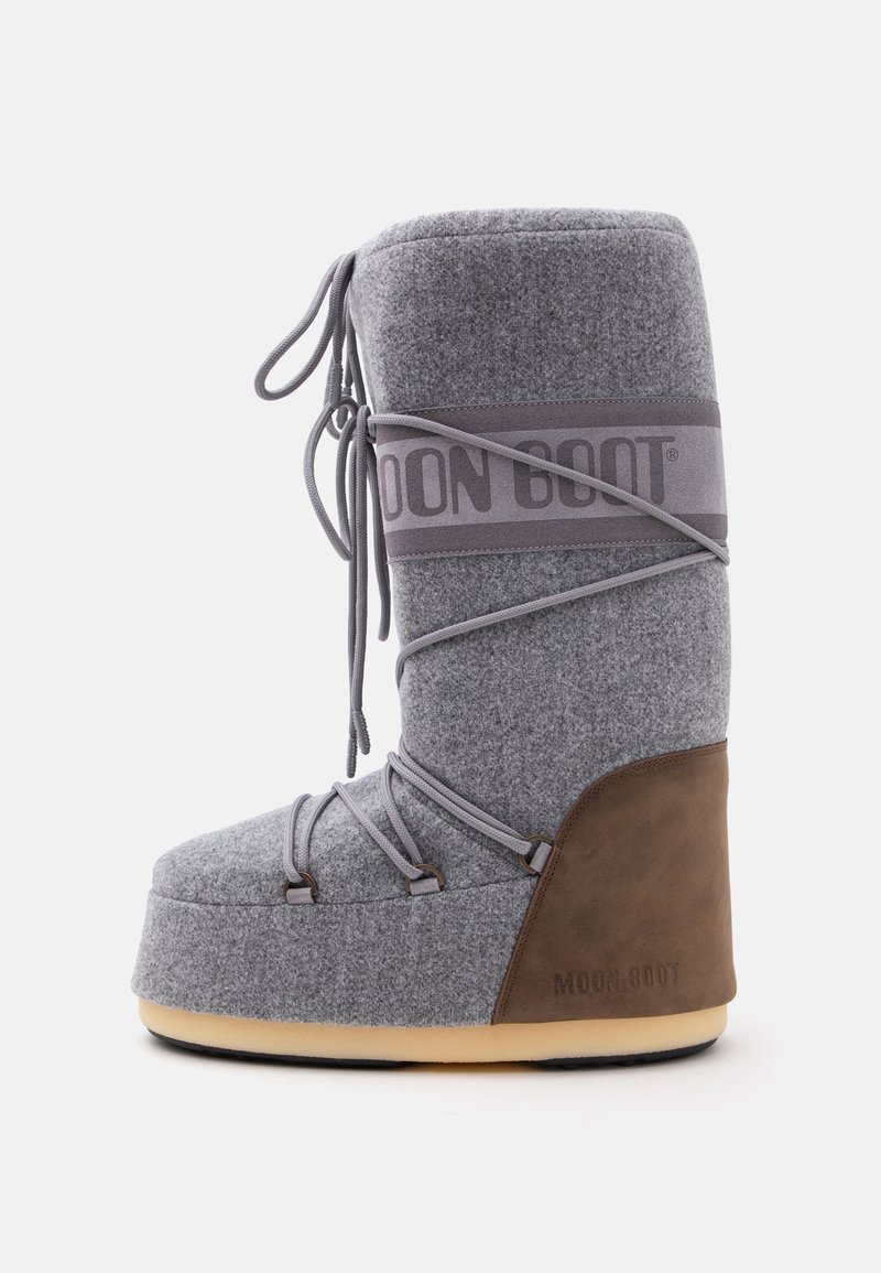 Botte d'hiver haute grise et marron avec une semelle épaisse et des lacets enveloppants, portant le nom de marque Moon Boot sur le côté.