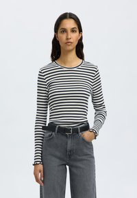 Camisola de mangas compridas à risca em tecido canelado azul marinho e branco, com decote redondo e punhos franzidos, combinada com jeans cinzentos de cintura alta e um cinto preto.